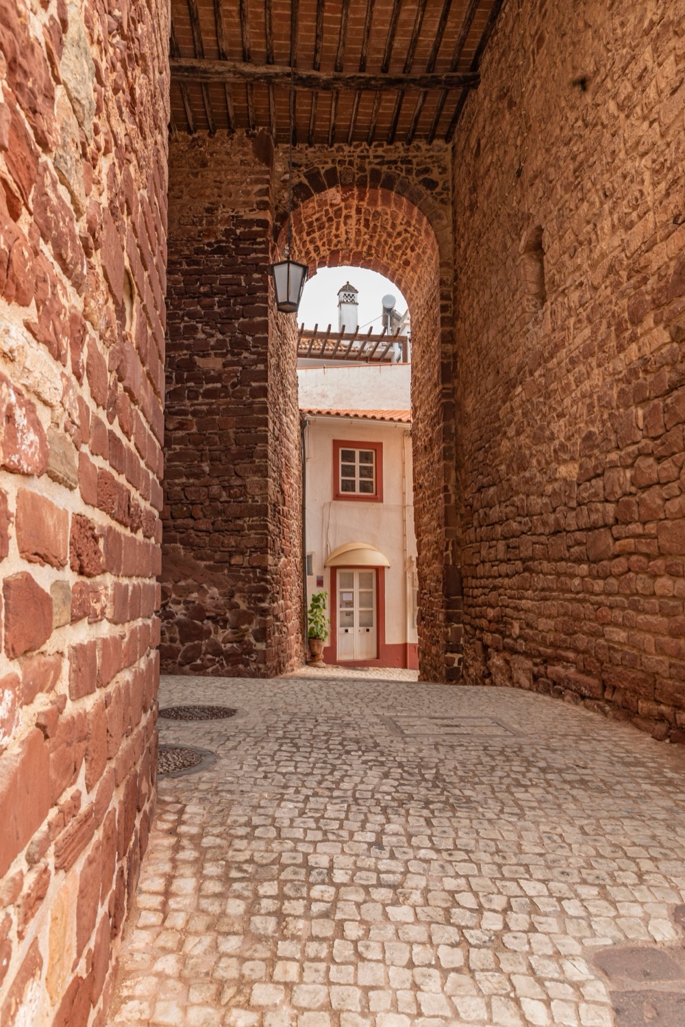 Arco de grés vermelho na muralha de Silves, com a rua em calçada por trás